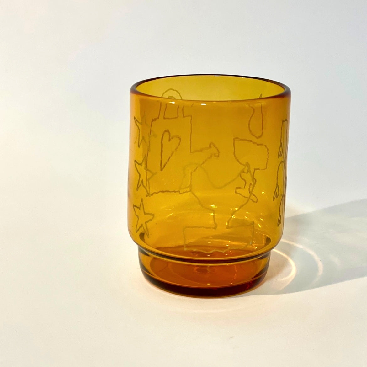 Glass tumbler with engravings of watering can, chicken, goblet, plant, and star motifs
