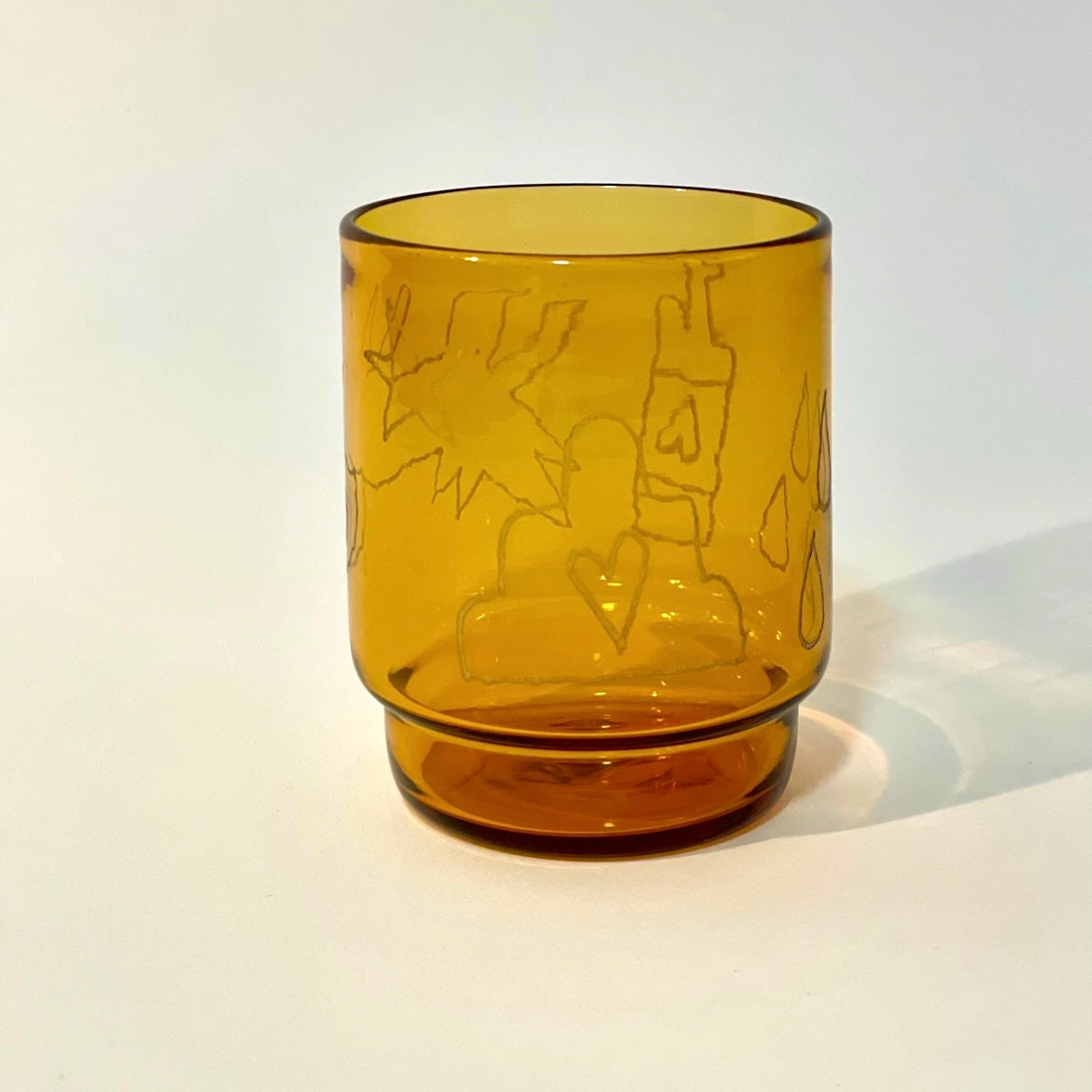 Glass tumbler engraved with a beehive, dog, bottle, and rain drop motifs