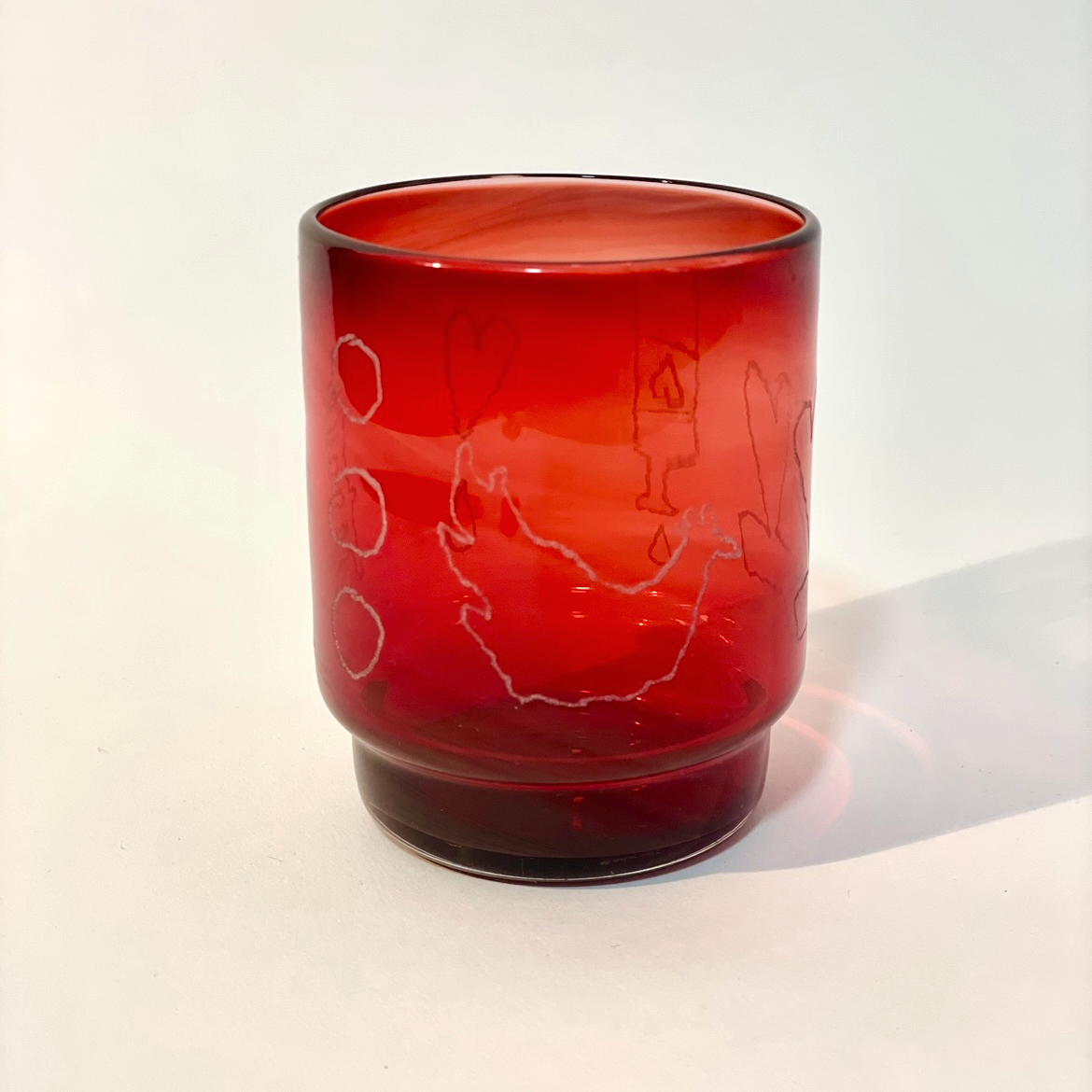ruby tumbler engraved with bottle, lovers, chicken, three coins, and ladder motifs.